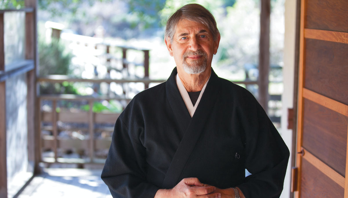 A man smiles and stands in black robes.