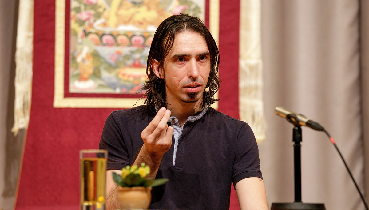 A man sitting in a tshirt in front of a microphone talking.