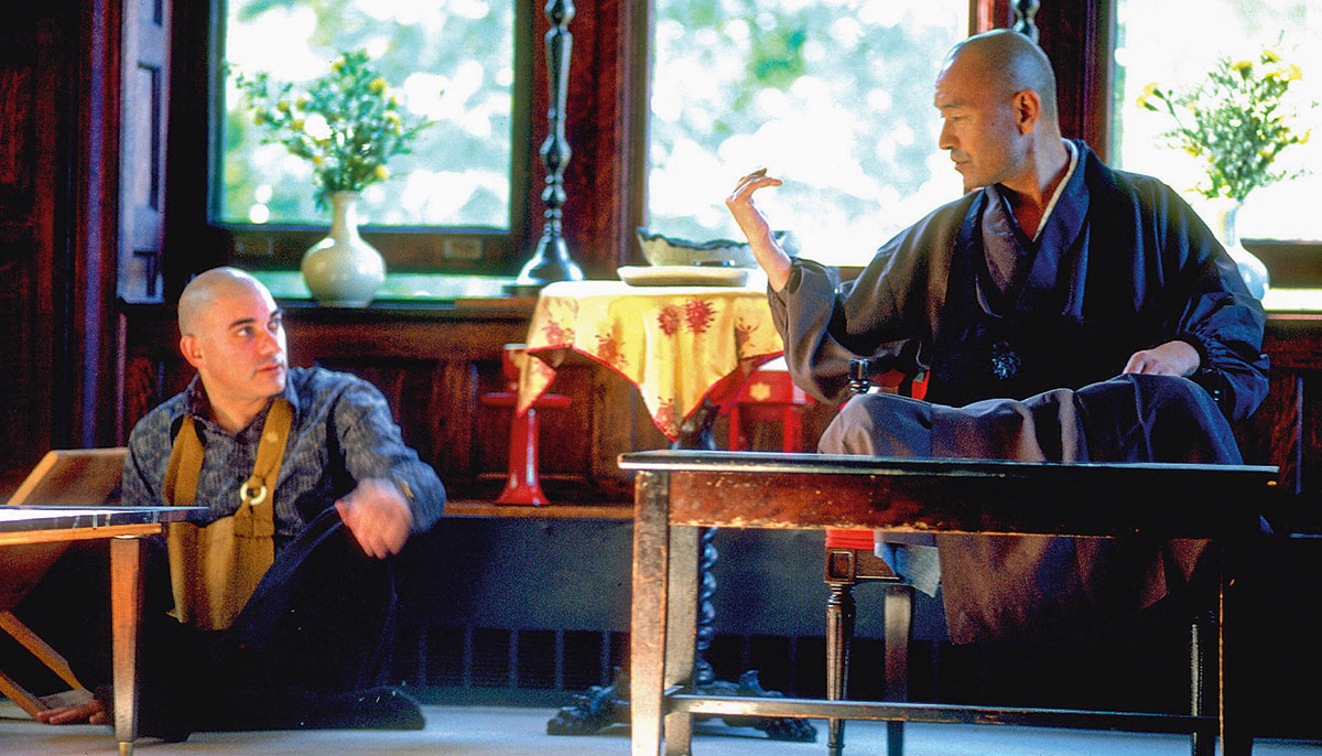 Two people looking at each other. One man is sitting on the ground and the other is sitting on a platform.