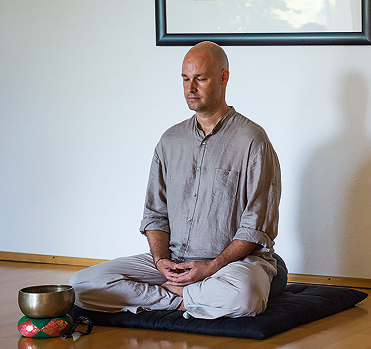 A man wearing grey clothes meditating.