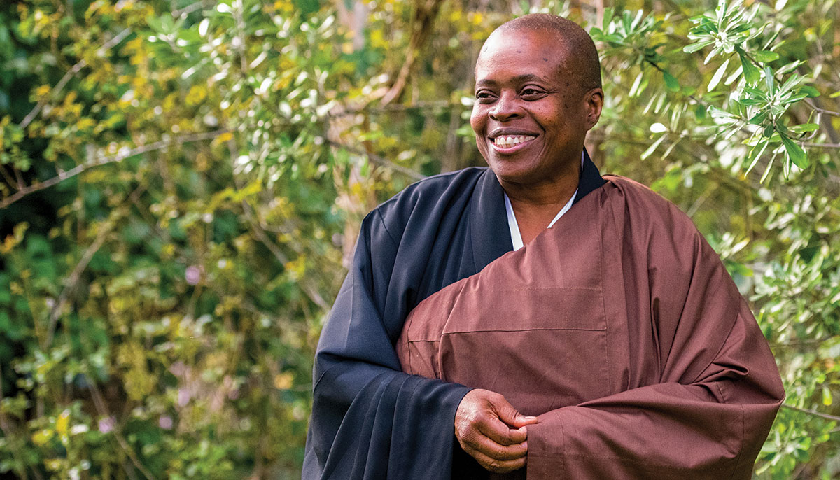 A woman wearing black robes with a maroon sash overtop. She is smiling.