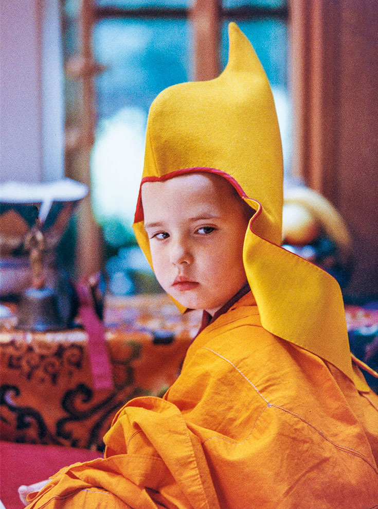 A young boy in yellow traditional robes and hat of a Tibetan Buddhist teacher.