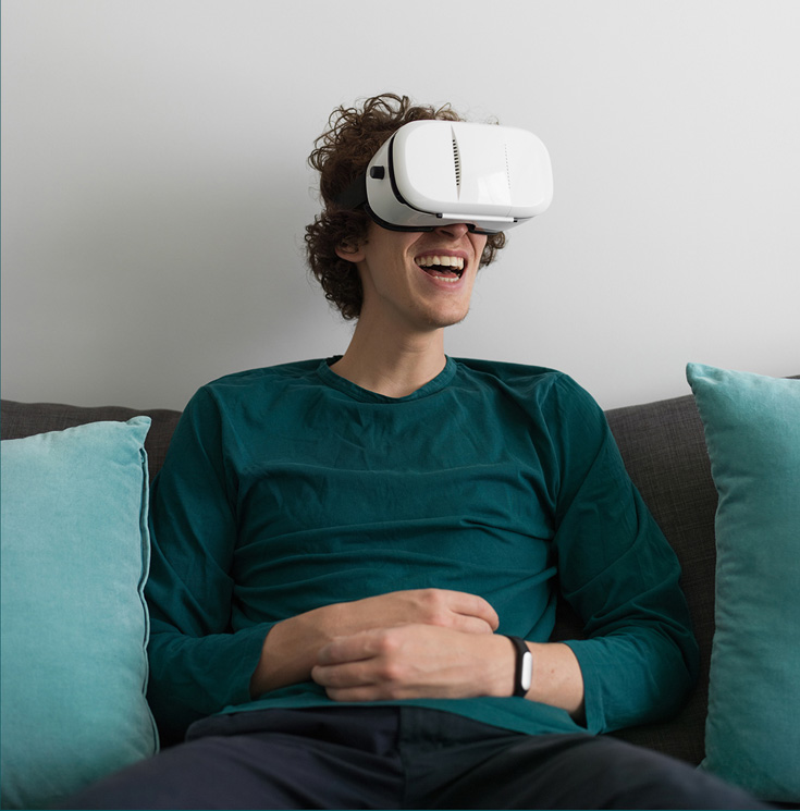 A man with a teal shirt wearing virtual reality goggles. He is smiling.