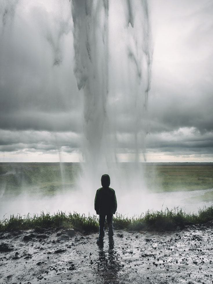 A young boy stands in front of a stream of water.