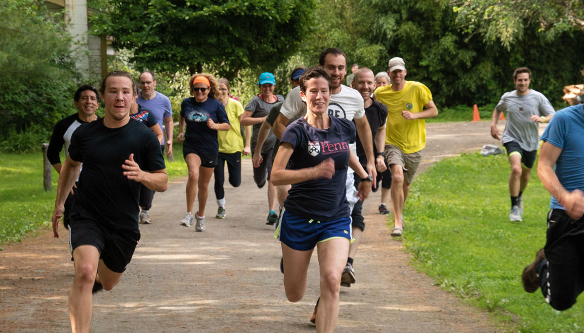 A pack of people all running on a path near grass.