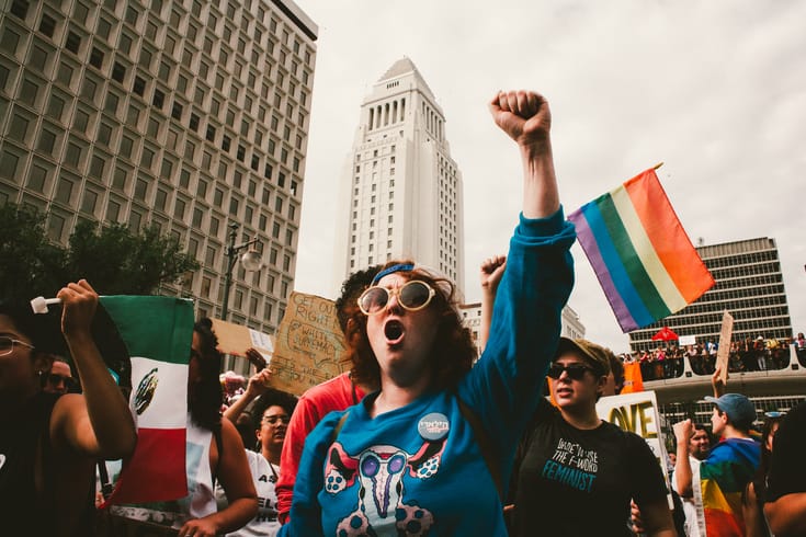 Anti-Trump protestor with Pride Flag in background.