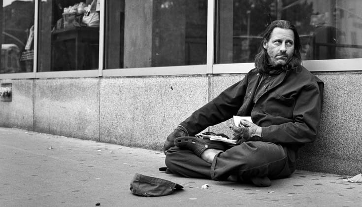 Man sitting in front of whole foods in zazen posture with hat on ground, begging for changing.