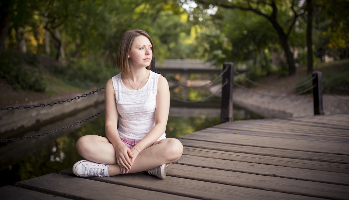 Woman sitting cross legged on the ground, looking into the distance.