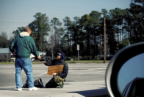 A man giving a homeless person some spare change.