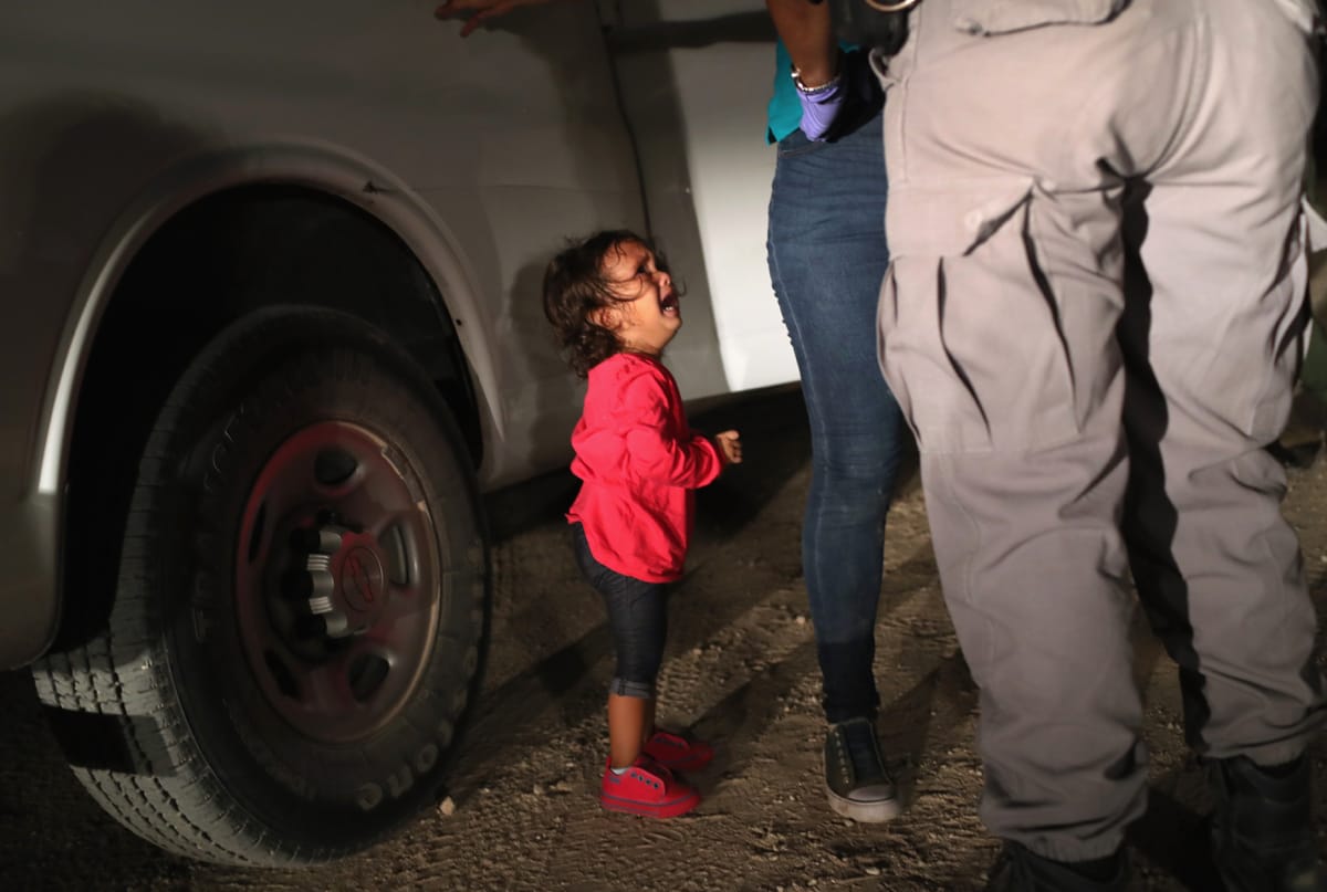 Small girl crying while border guards search her mother.