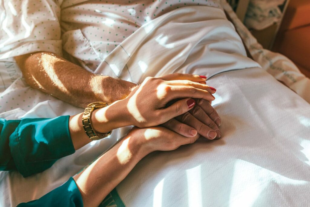 A woman holding a man's hand in a hospital bed.