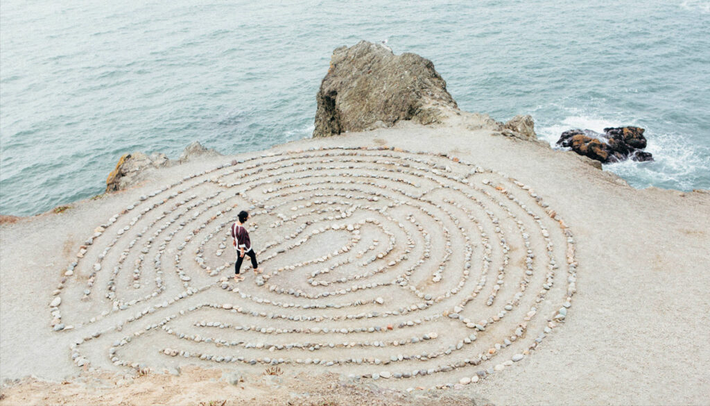 A man walks a labyrinth made of stones next to the ocean