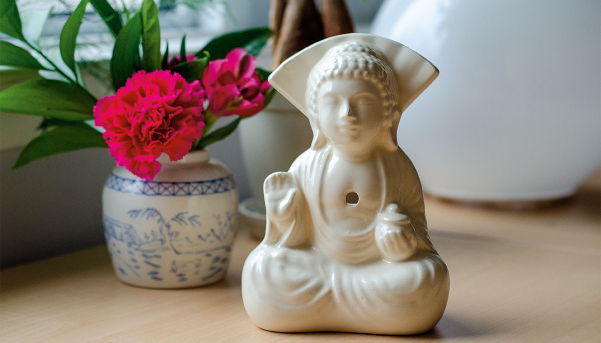 Ceramic buddha cup with red flowers in background.