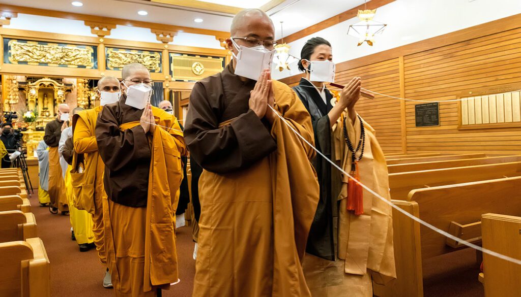 People in robes walking. Their hands are folded in a praying motion and they are all standing.