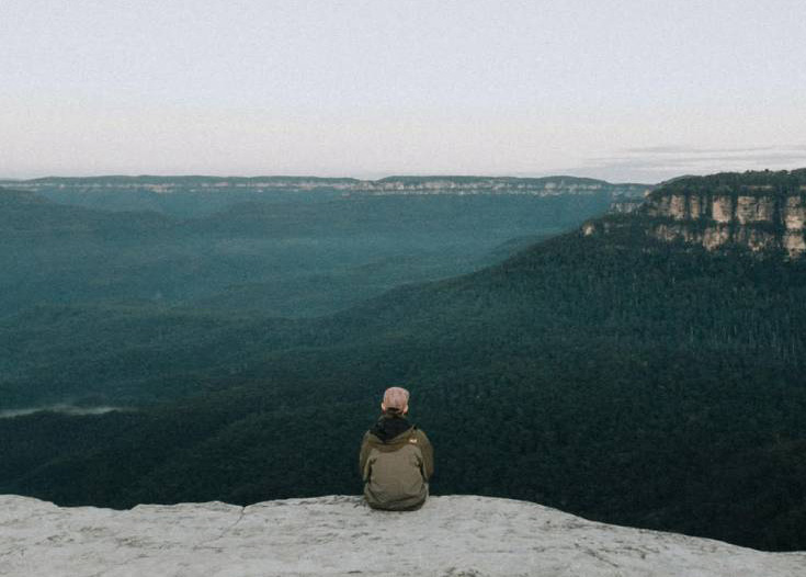 Man sitting on cliff overlooking mountain range