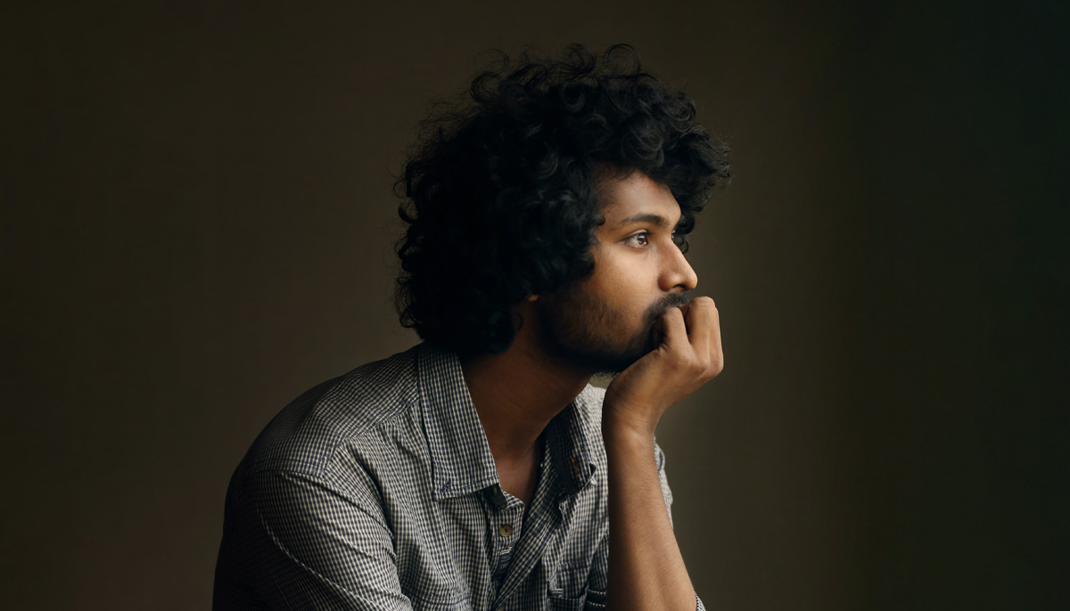 Man with curly hair sits in thought resting his chin in his hand.