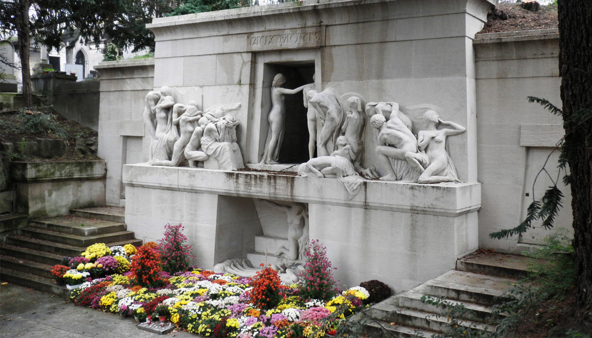 A momunment at Père Lachaise Cemetery reads "Aux Morts," or "to the dead," with stautes of people surrounded by flowers.