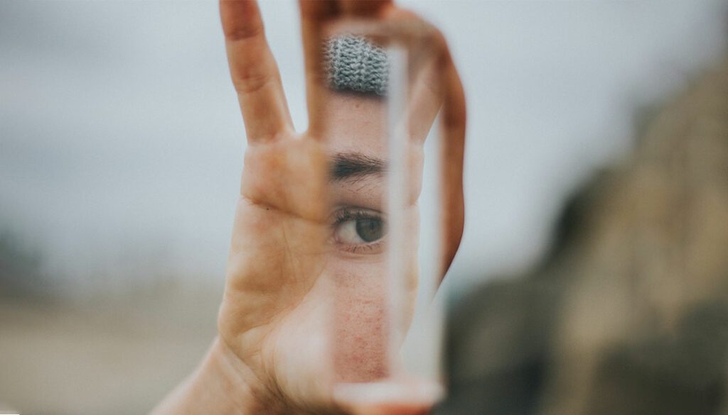 A hand holds a mirror, reflecting an eye looking back at itself.