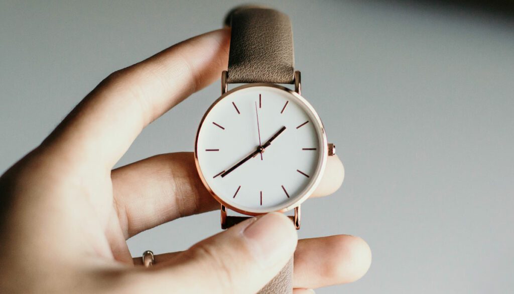 Hand holding a gold wrist watch with a brown leather strap