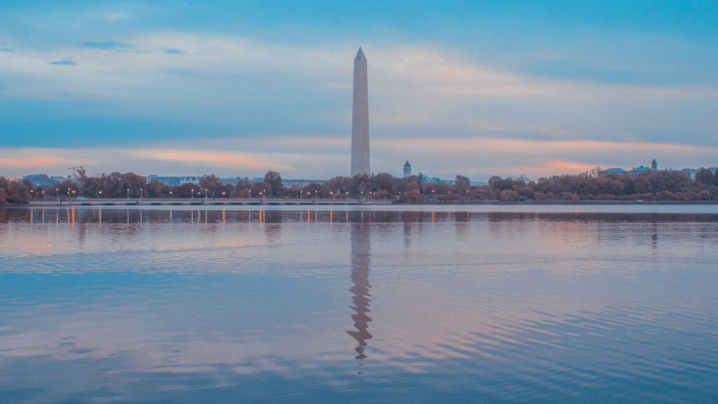 The washington monument reflects on water in front of a blue and pink sky