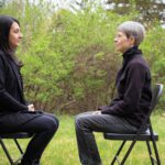 Two people sitting outside on folding chairs facing each other