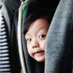 image of a little boy peeping out of hung clothes in closet.