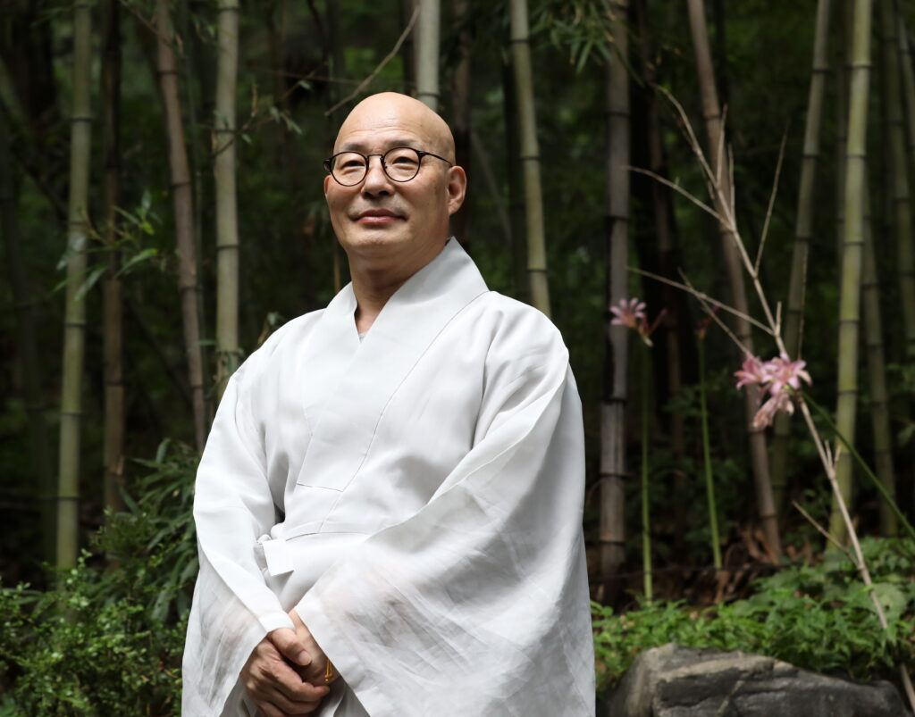Monk Jin Woo is pictured standing and smiling.
