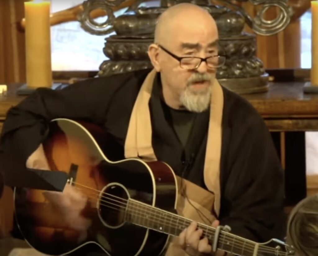 Alan Senauke is seen playing guitar and singing.