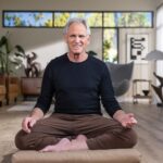 Jon kabat-zinn sitting cross-legged, smiling at the camera.