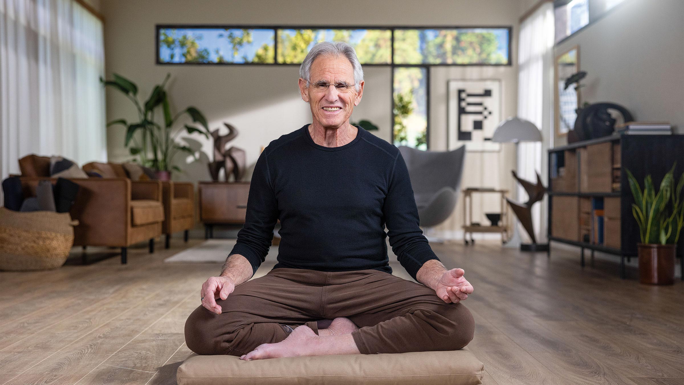 Jon kabat-zinn sitting cross-legged, smiling at the camera.
