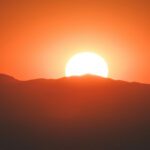 An orange sun rises over a mountain range.