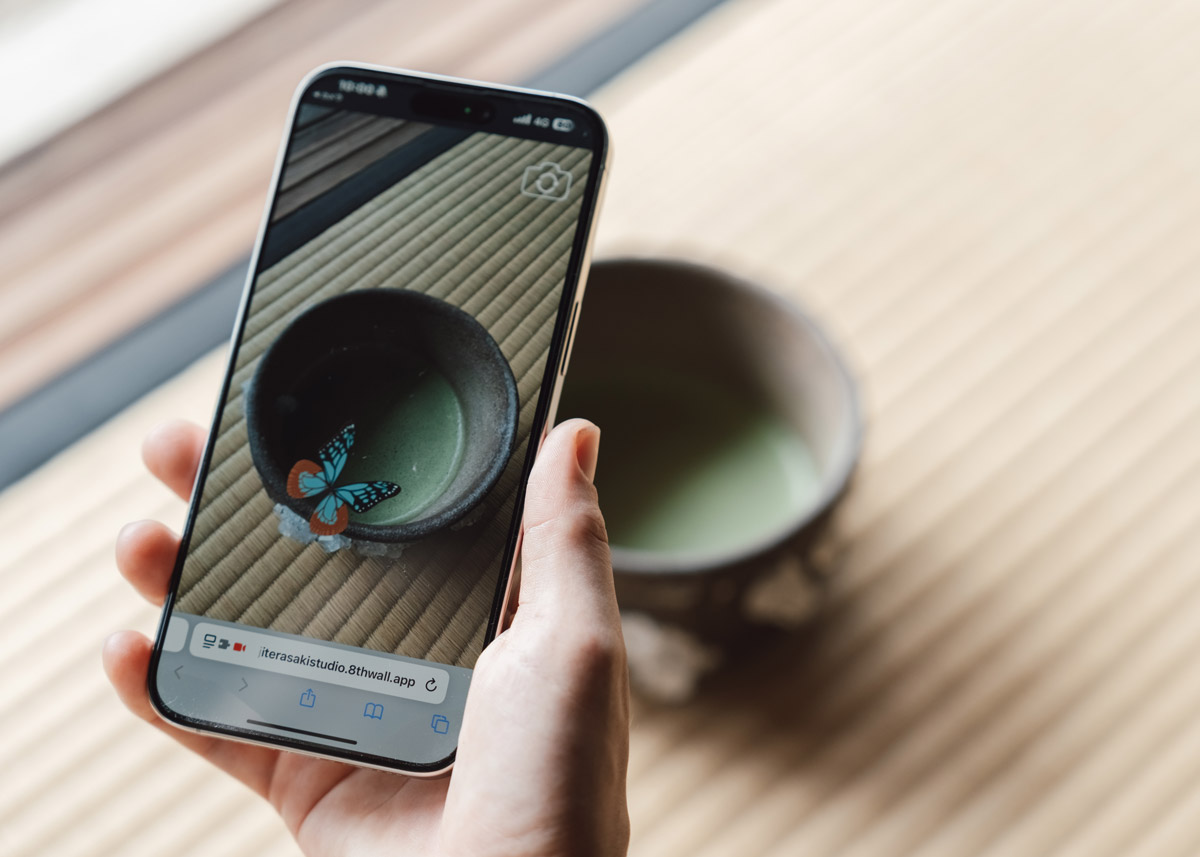 A person holding a smart phone with a butterfly image in it over a cup of matcha tea