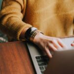 woman in yellow sweater types on a laptop