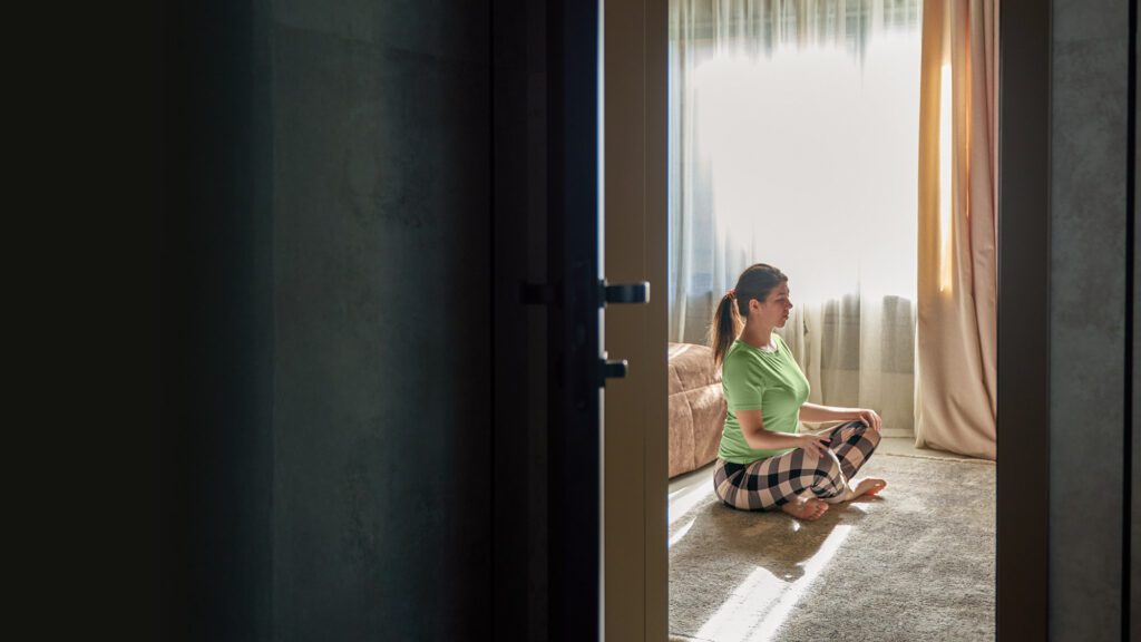 Opened door reveals a woman in sitting meditation posture in her room.