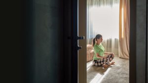 Opened door reveals a woman in sitting meditation posture in her room.